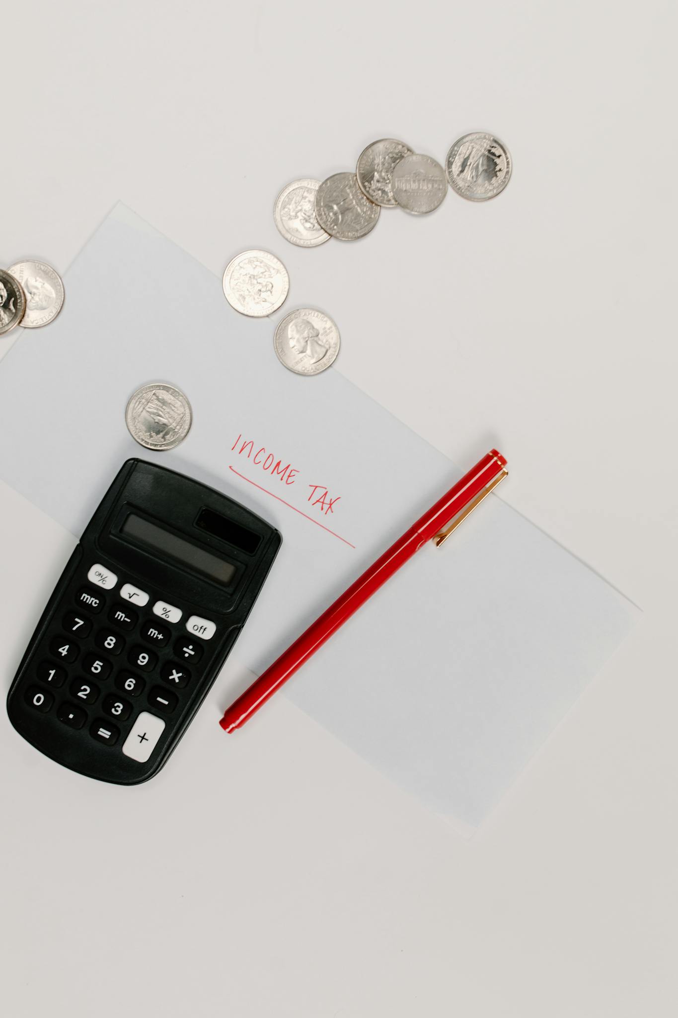 Calculator, pen, and coins on an envelope labeled 'Income Tax' for tax preparation.
