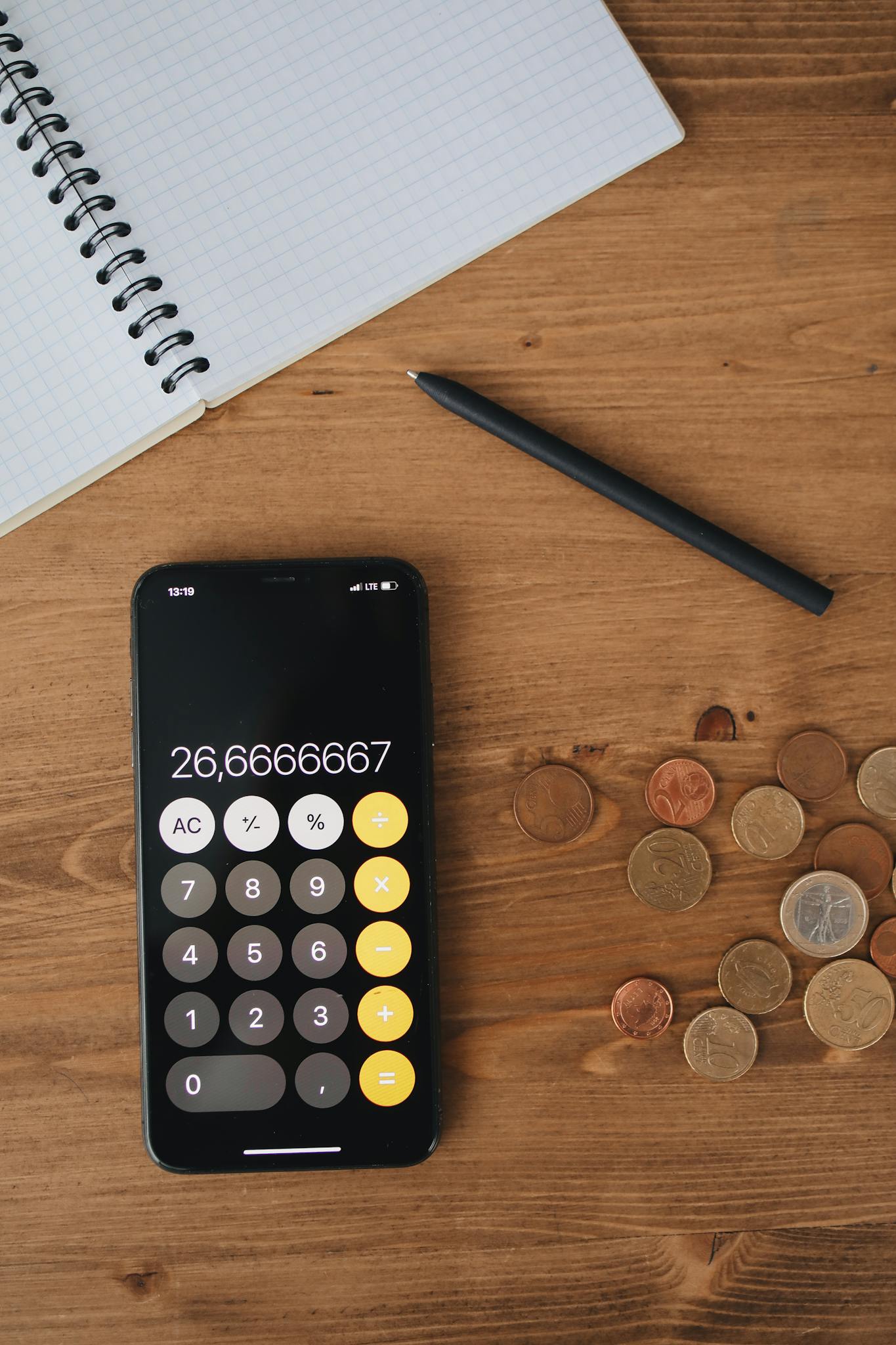 Top view of a smartphone calculator, coins, notebook, and pen on a wooden table for financial concept.